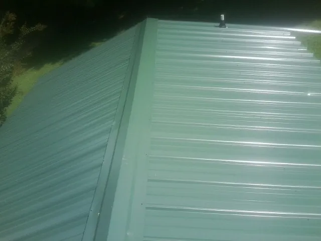New green metal panels meeting at the ridge of a roof — Flat Roof Repair work by our crew in Branchville